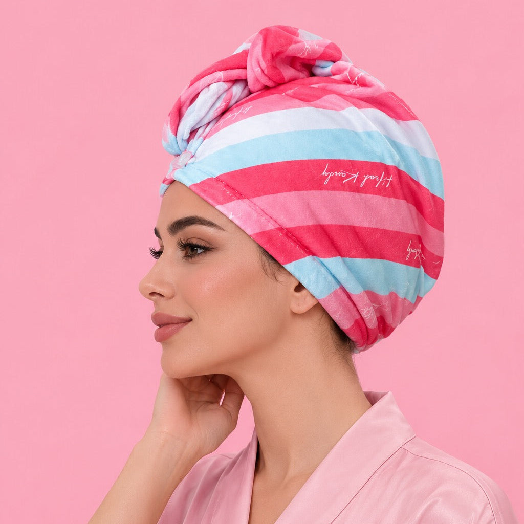 A woman in a pink satin robe wearing a pink, light blue, and white striped cotton turban hat, posed against a solid pink background.