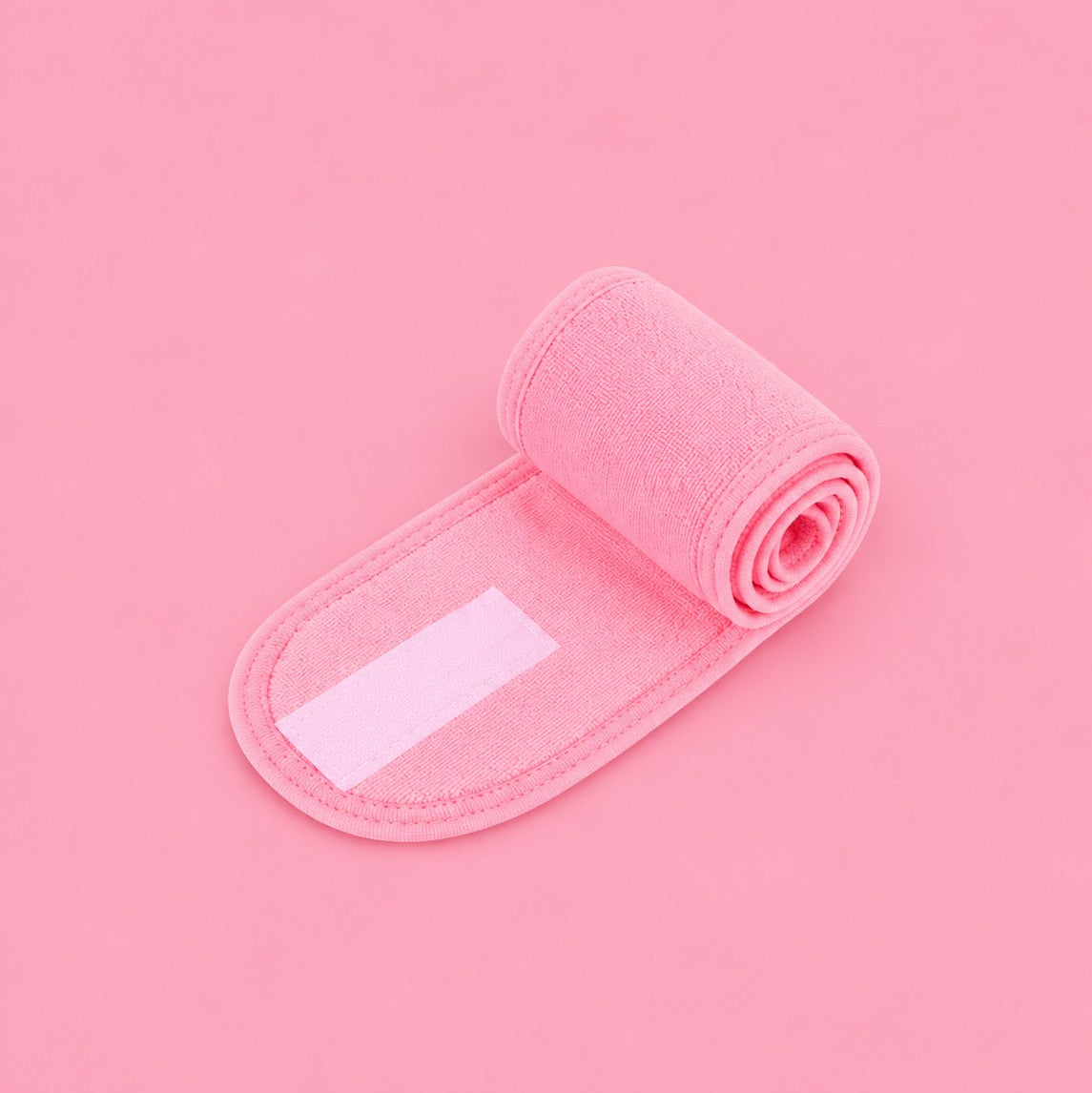 A pink rolled-up fabric strap or band with a rectangular white patch, photographed on a solid pink background.