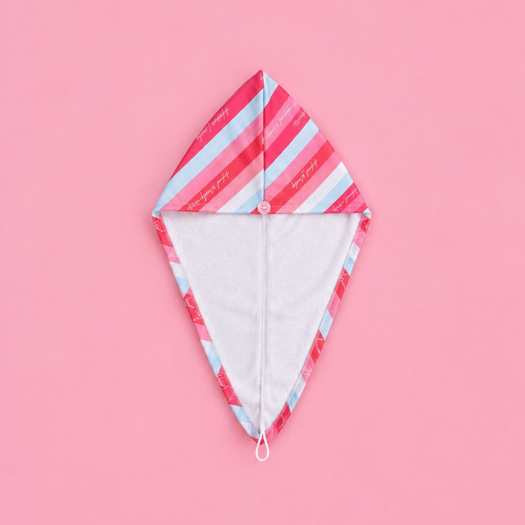 A diamond-shaped hooded towel or pouch with a pink and light blue diagonal striped pattern on the outside and a white fabric lining on the inside, displayed on a solid pink background.
